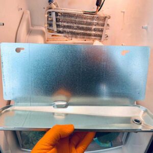 A person holding a metal sheet in front of a stainless steel refrigerator.