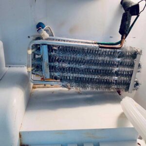 A damaged refrigerator evaporator with tinsel wrapped around it, sitting on top of a refrigerator door.